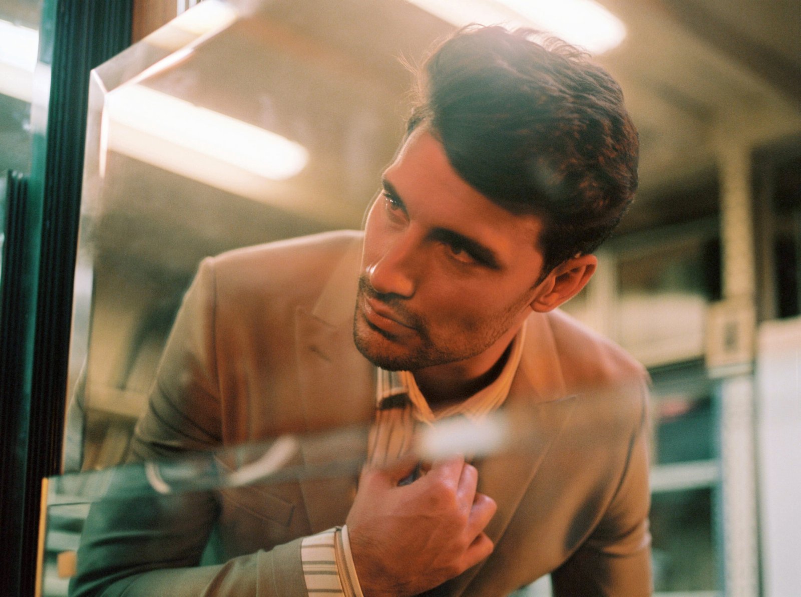 Close-up editorial portrait of Jaime Astrain through reflective glass wearing beige tailoring styled by Júlia Puñet