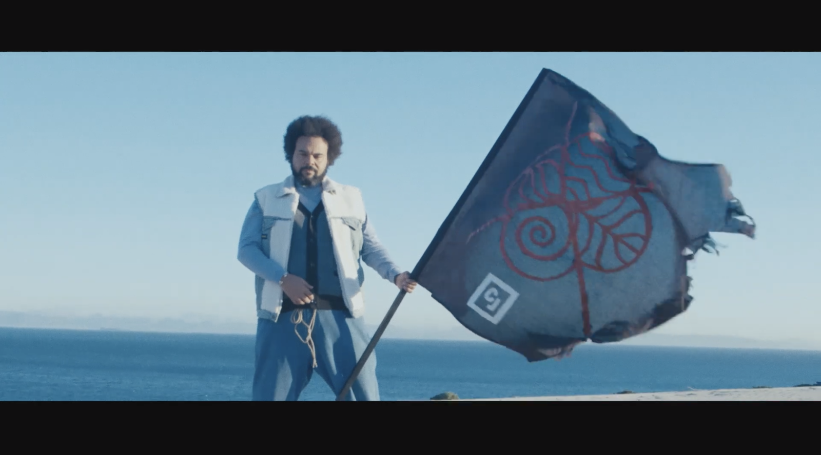 Carlos Jean standing with a black symbolic flag during the filming of the “Downtown” music video.
