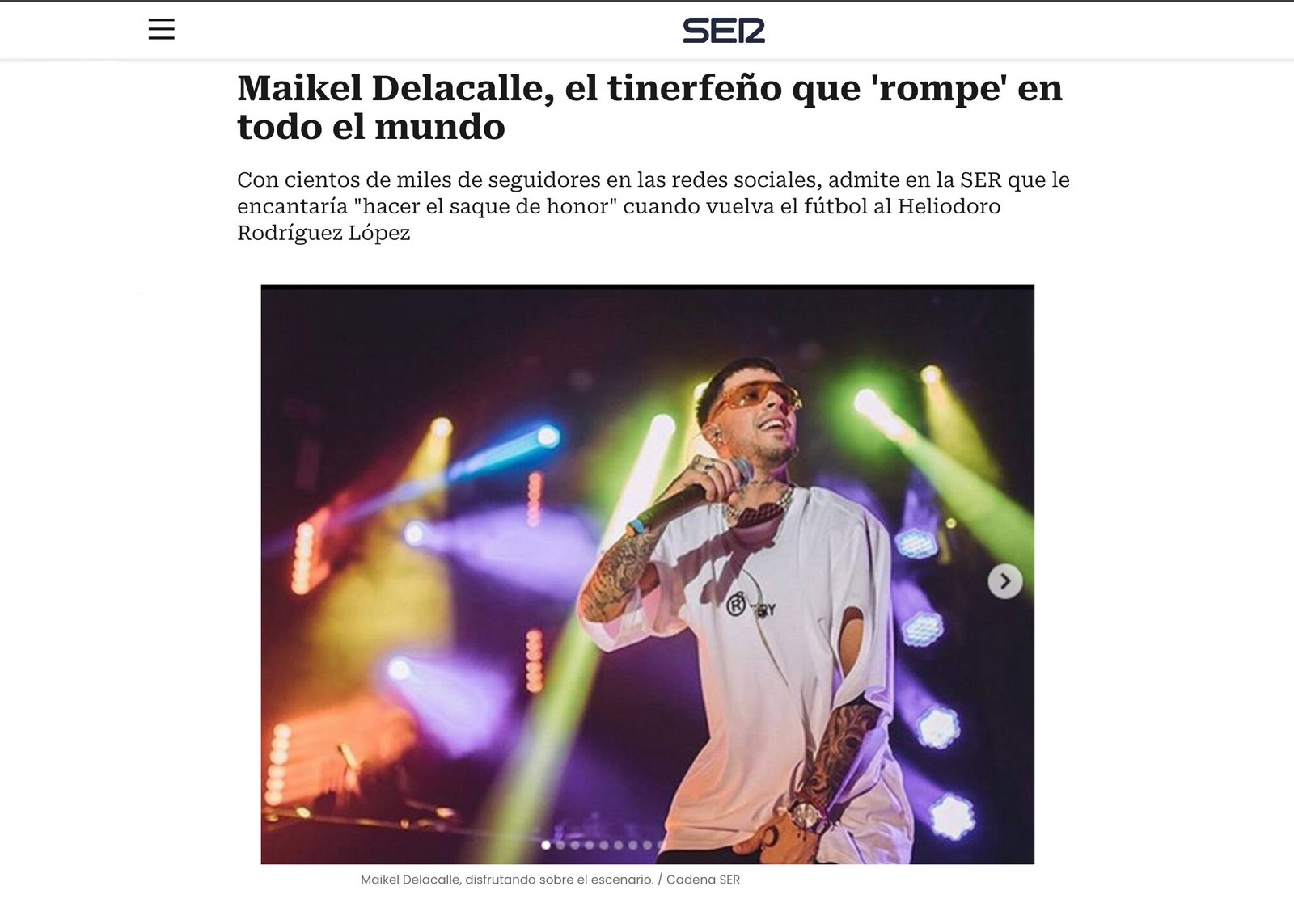 Maikel De la Calle performing live on stage wearing black graphic t-shirt under intense yellow and blue concert lights